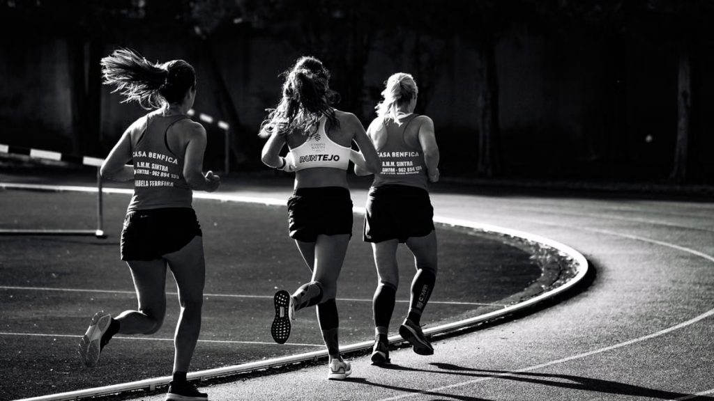 Black and white back view of unrecognizable fit female runners in sportswear running during track and field competition