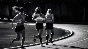 Black and white back view of unrecognizable fit female runners in sportswear running during track and field competition